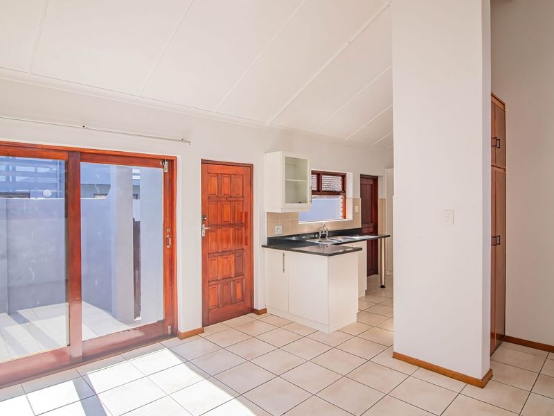 Open plan living area featuring tiled floors, vaulted ceilings, and a functional kitchen with built-in cabinetry, leading out to a private patio area.