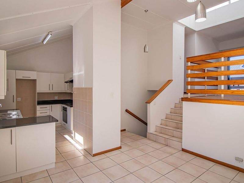 Open-plan kitchen featuring white cabinetry, granite countertops, and tiled flooring, adjacent to a staircase with a wooden balustrade and a bright skylight.