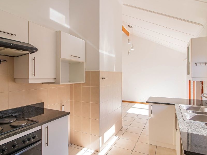 A bright, functional kitchen featuring white cabinetry, granite countertops, built-in oven and hob, and tiled finishes, leading into an open-plan living area.