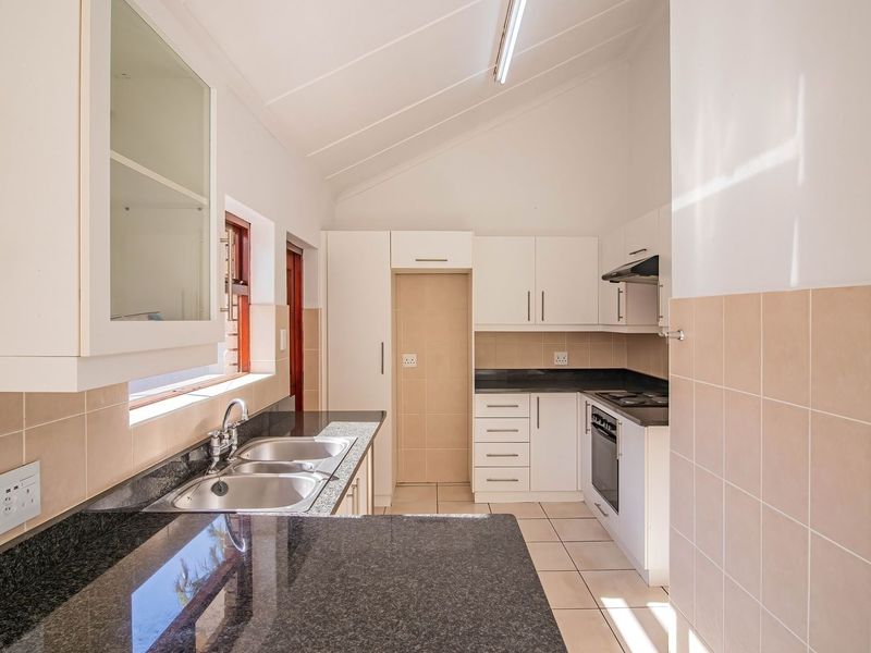 A clean, functional kitchen featuring granite countertops, built-in oven and hob, tiled backsplash, and ample cabinetry under a vaulted ceiling.
