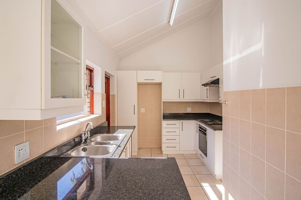 A clean, functional kitchen featuring granite countertops, built-in oven and hob, tiled backsplash, and ample cabinetry under a vaulted ceiling.