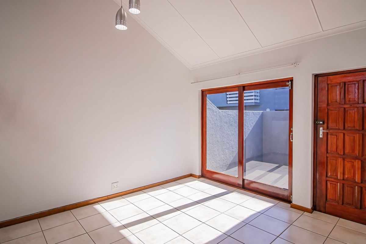 Bright, empty living area featuring tiled floors, a vaulted ceiling, and sliding glass doors providing access to an outdoor patio space.
