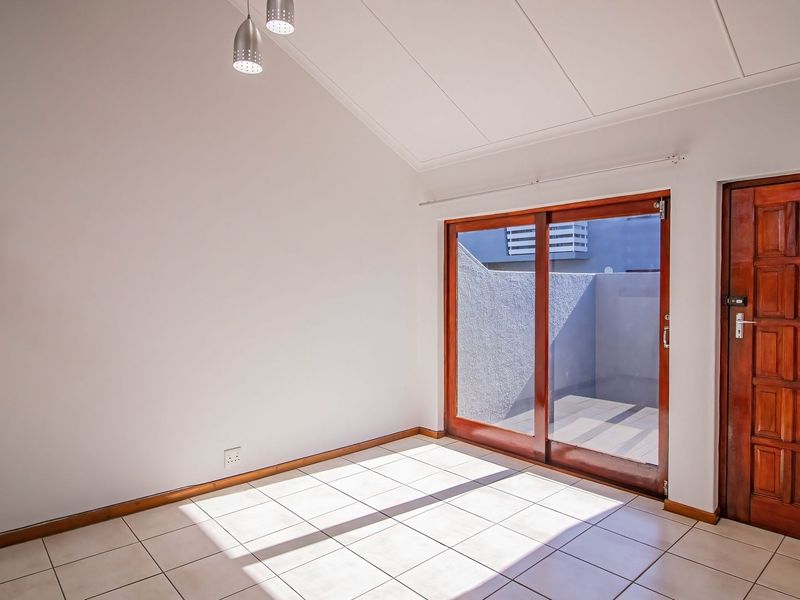 Bright, empty living area featuring tiled floors, a vaulted ceiling, and sliding glass doors providing access to an outdoor patio space.