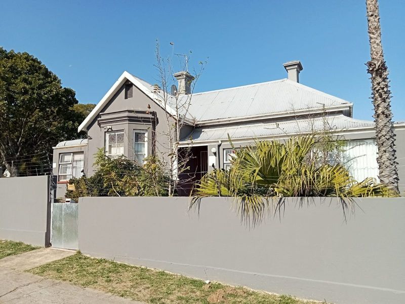 Front exterior view of a guest house featuring a corrugated metal roof, chimney stacks, and a secure perimeter wall with electric fencing.