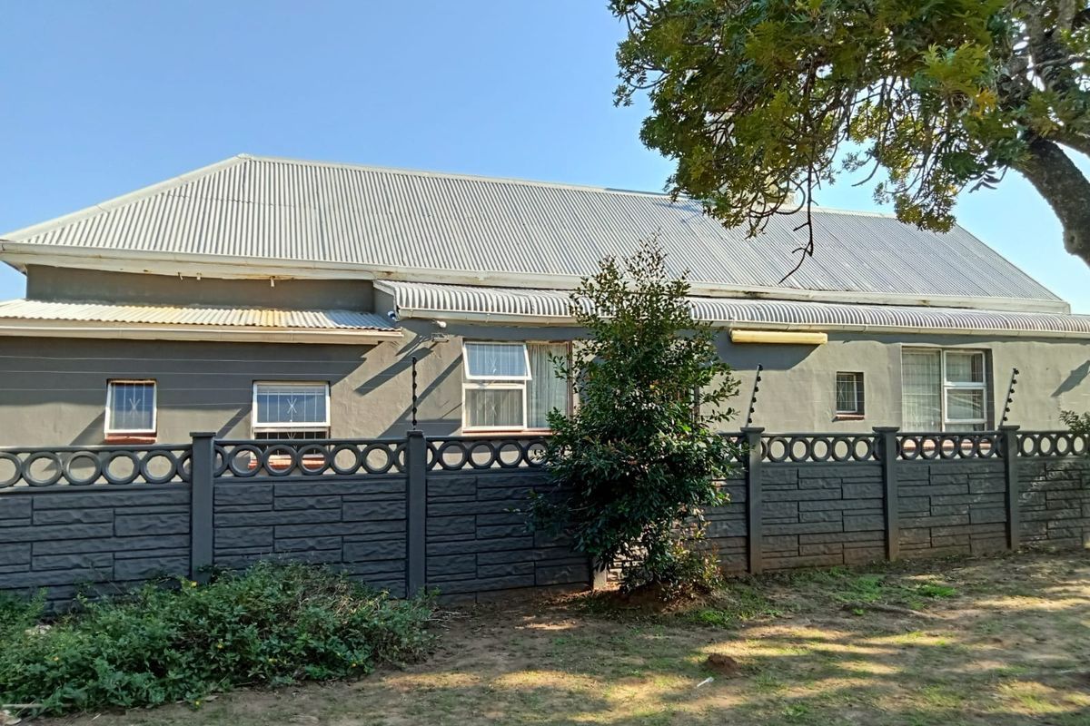 Rear exterior view of the guest house featuring a corrugated metal roof, grey painted walls, and a secure precast concrete boundary wall with electric fencing.