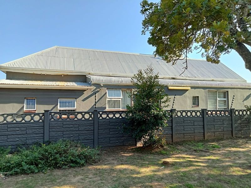 Rear exterior view of the guest house featuring a corrugated metal roof, grey painted walls, and a secure precast concrete boundary wall with electric fencing.