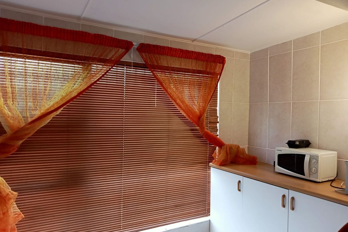 A functional kitchen area featuring white built-in cabinetry, a laminate countertop, and tiled wall finishes, complemented by venetian blinds.