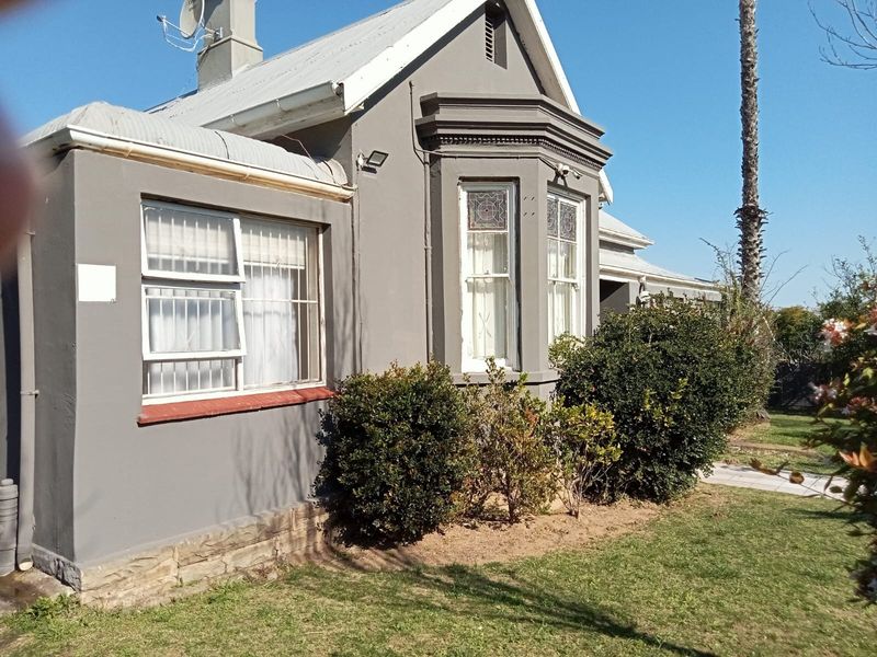 Front elevation of a guest house featuring a bay window, corrugated metal roof, and stone foundation detailing, set within a landscaped garden.