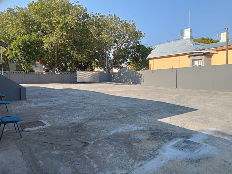 A spacious, paved outdoor area featuring a perimeter wall with security fencing and a gated entrance, suitable for parking or utility use.