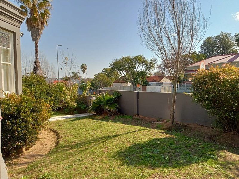 A view of the rear garden area featuring a perimeter wall, paved walkway, and established landscaping.