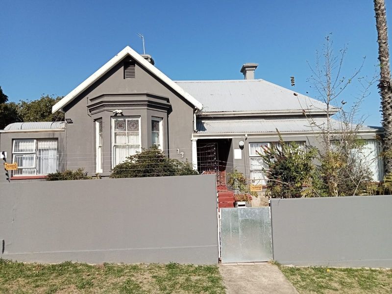 Front elevation of a guest house featuring a corrugated metal roof, bay window, and secure perimeter wall with electric fencing.