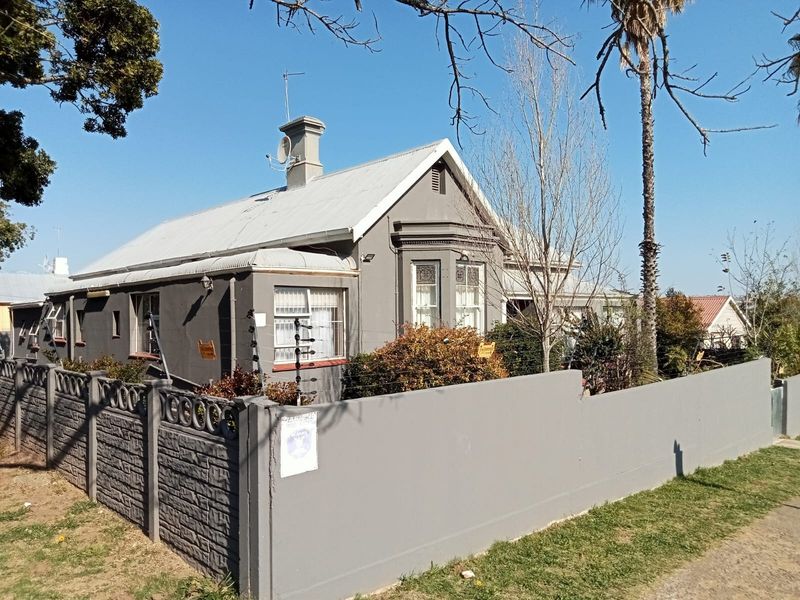 Front elevation of a single-story guest house featuring a corrugated metal roof, bay window, and a secure perimeter wall with electric fencing.