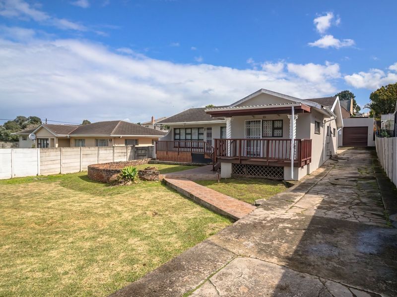 Rear view of the property featuring a raised timber deck, a concrete driveway, and a spacious garden enclosed by precast concrete boundary walls.