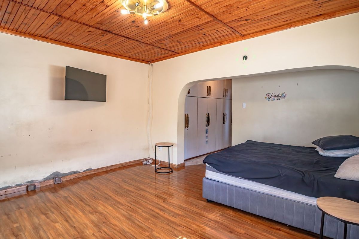 Bedroom featuring timber ceiling, laminate flooring, and built-in cupboards, with an arched transition to a storage area.