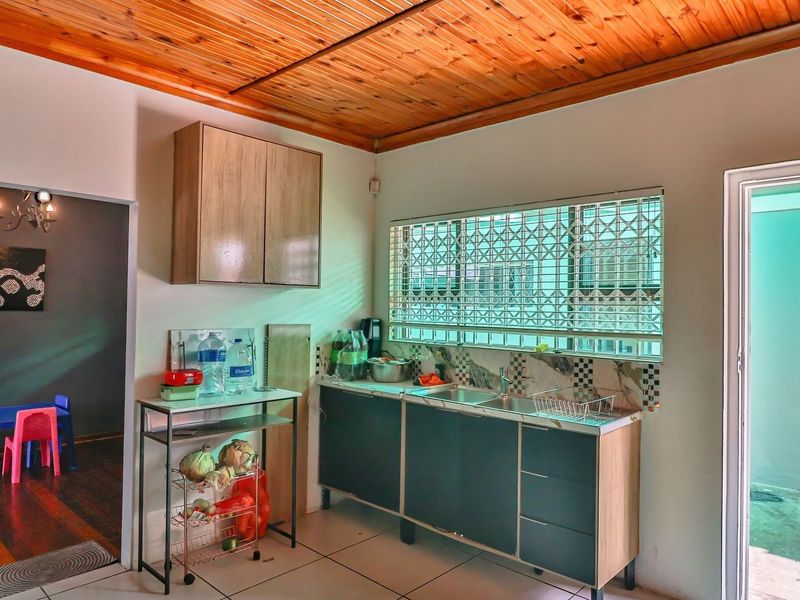 A functional kitchen area featuring timber ceiling paneling, built-in cabinetry, a stainless steel sink, and tiled flooring with access to an outdoor area.
