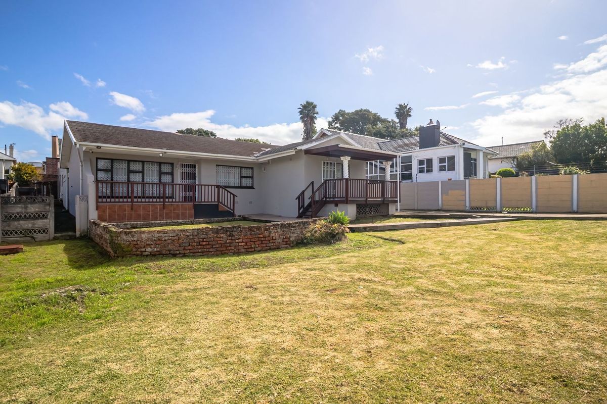 Rear view of the property featuring a spacious lawn, raised timber deck, and brick retaining wall, enclosed by a perimeter boundary wall.