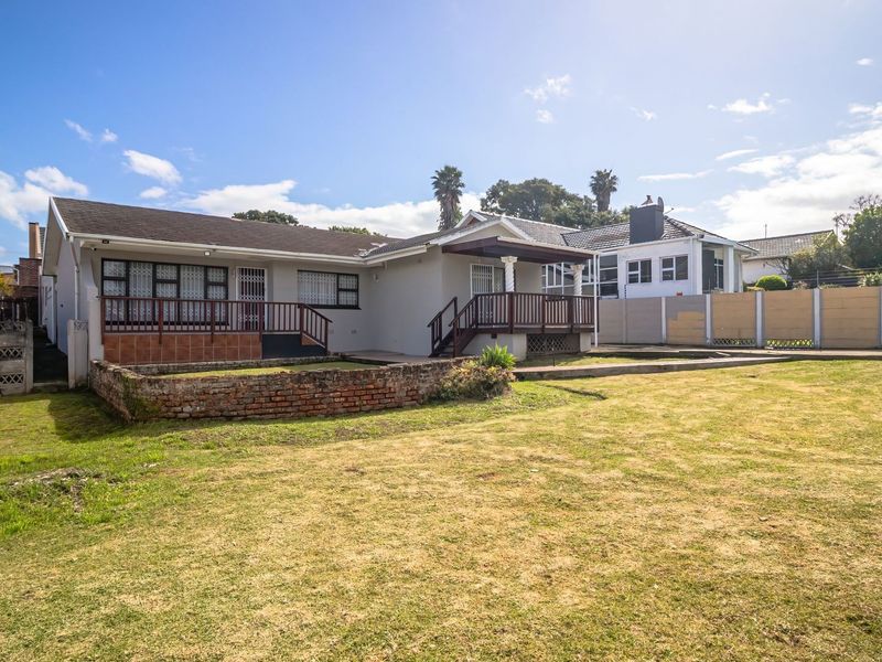 Rear view of the property featuring a spacious lawn, raised timber deck, and brick retaining wall, enclosed by a perimeter boundary wall.