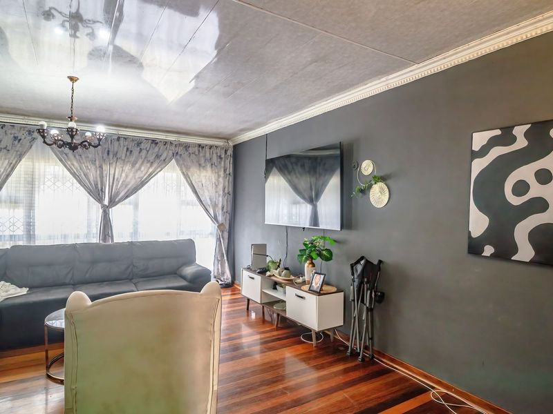 A living room featuring polished hardwood flooring, crown molding, and a ceiling rose, with a dark accent wall and large windows.