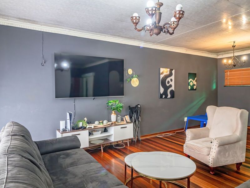 A living room featuring hardwood flooring, crown molding, and a decorative chandelier, with dark grey walls and visible ceiling finishes.