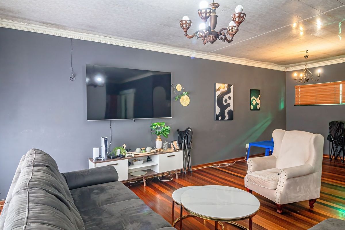 A living room featuring hardwood flooring, crown molding, and a decorative chandelier, with dark grey walls and visible ceiling finishes.