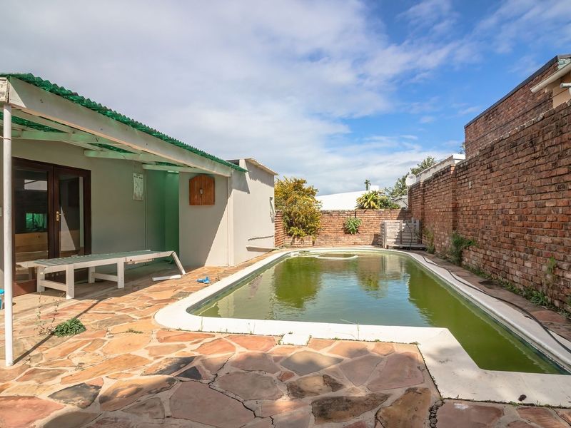 Outdoor pool area featuring a paved patio, covered veranda, and brick boundary walls, currently requiring maintenance and pool water treatment.
