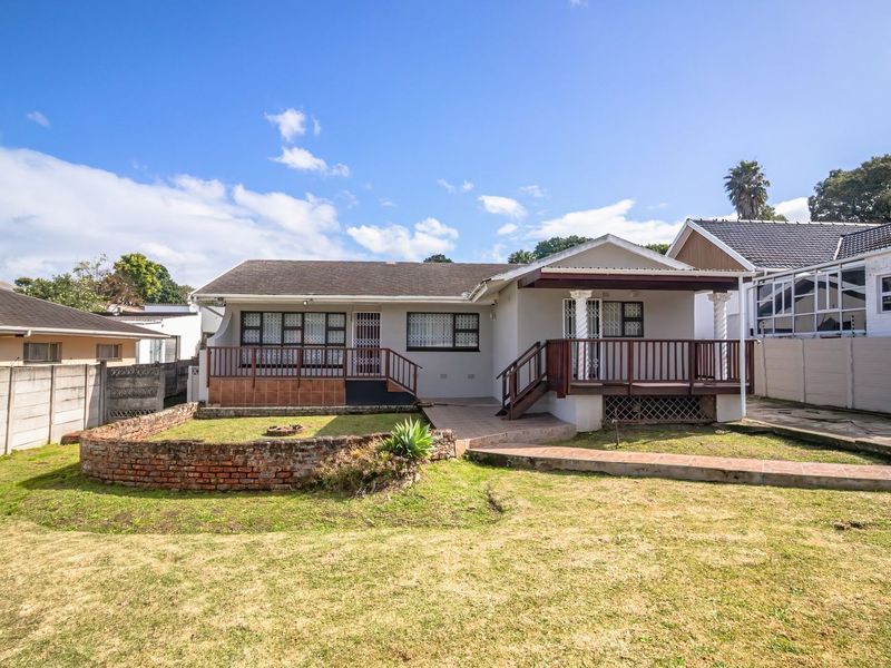 Rear view of the house featuring a raised timber deck, tiled patio area, and a brick retaining wall set within a private garden.