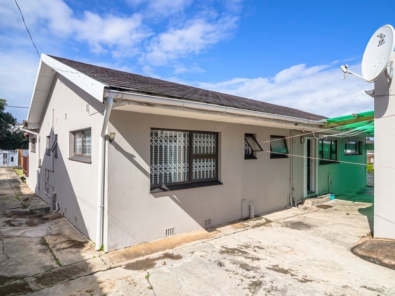 Rear exterior view of the house featuring a concrete driveway, security bars on windows, and a satellite dish installation.