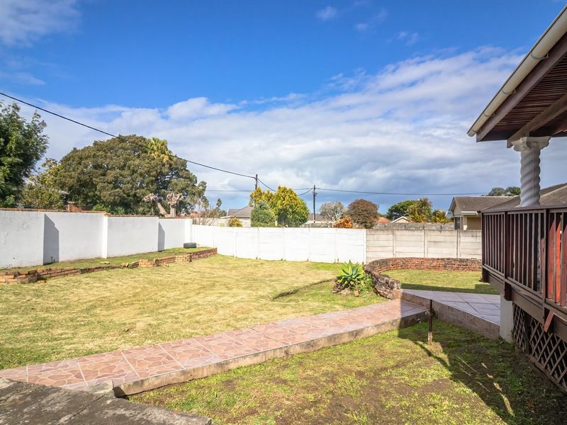 A spacious rear garden featuring a raised wooden deck, a tiled pathway, and secure perimeter walling, offering potential for outdoor landscaping and entertainment.