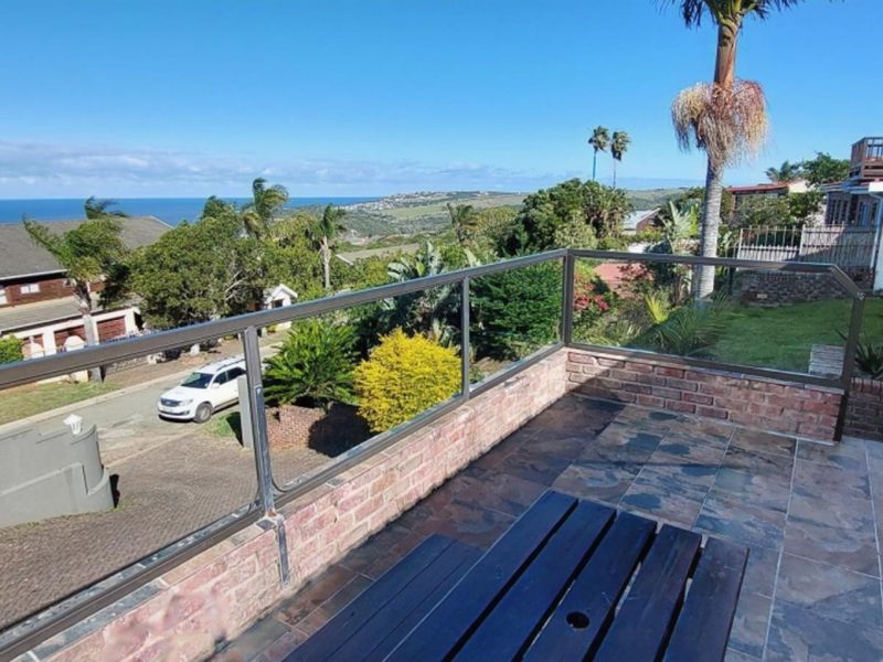 An elevated balcony featuring a glass balustrade, brick walling, and tiled flooring, offering expansive coastal and neighborhood views.