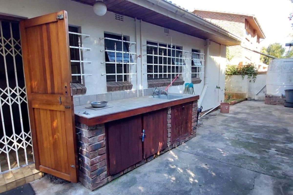 Rear exterior area featuring a brick-built outdoor counter with sink, security gates, and a water tank, set against a paved courtyard.