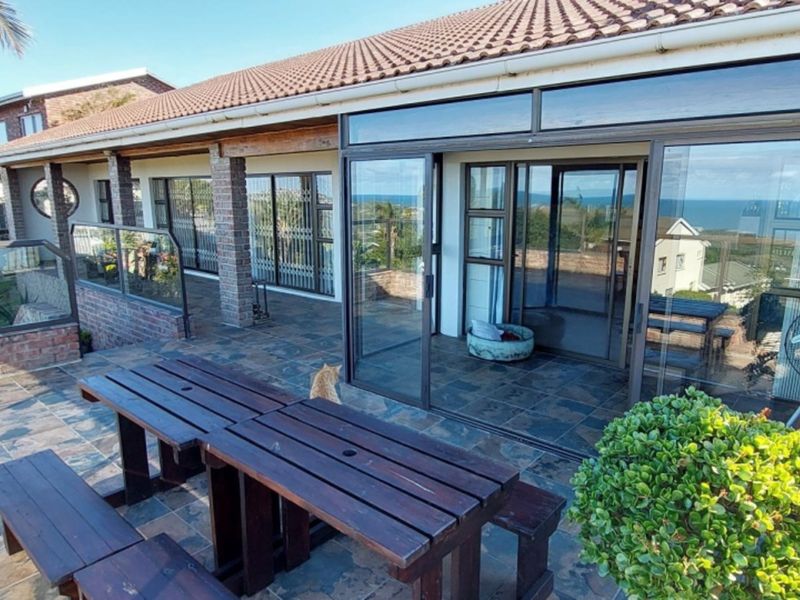 Spacious covered patio featuring tiled flooring, brick pillars, and large sliding glass doors, offering an outdoor entertainment area with scenic views.