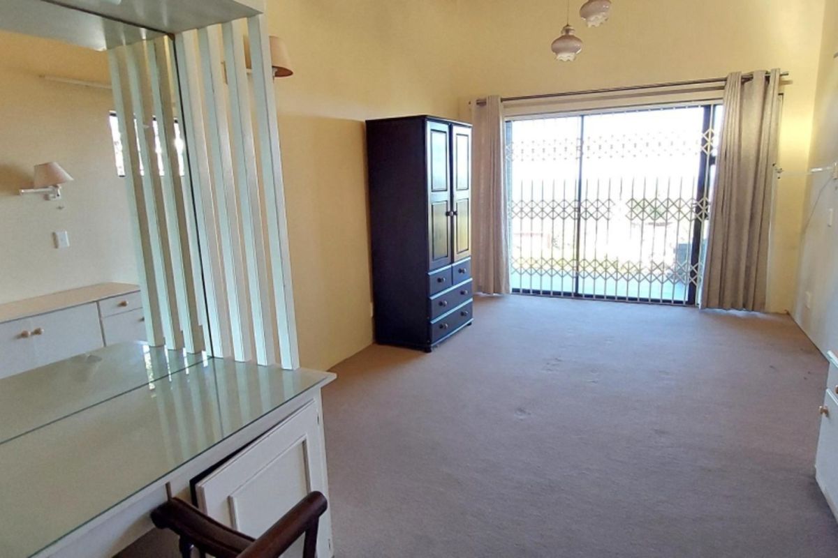 Spacious bedroom featuring built-in vanity and cabinetry, carpeted flooring, and a sliding glass door with security gate leading to the exterior.