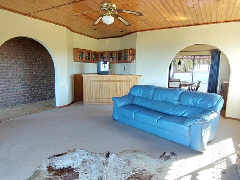Spacious living room featuring a timber ceiling, built-in bar, and a brick fireplace, offering a traditional layout with arched transitions to adjacent areas.