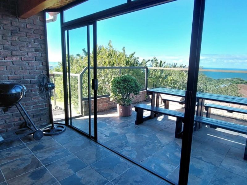 Covered patio area featuring exposed brick walls, tiled flooring, and sliding glass doors leading to a balcony with scenic ocean views.