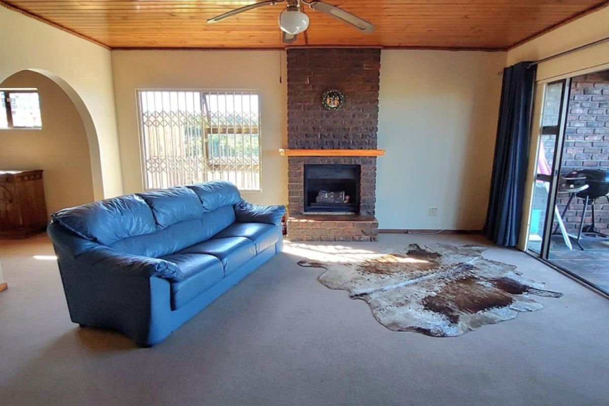 Spacious living room featuring a brick fireplace, timber ceiling, and large sliding glass doors providing access to the outdoor area.