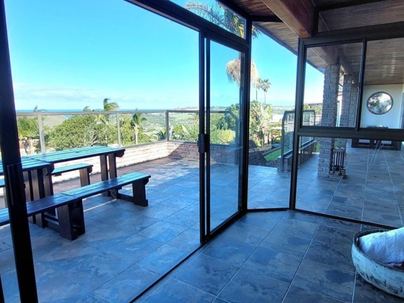 Spacious covered patio featuring tiled flooring, brick pillars, and large sliding glass doors that open to a scenic outdoor balcony with a glass balustrade.