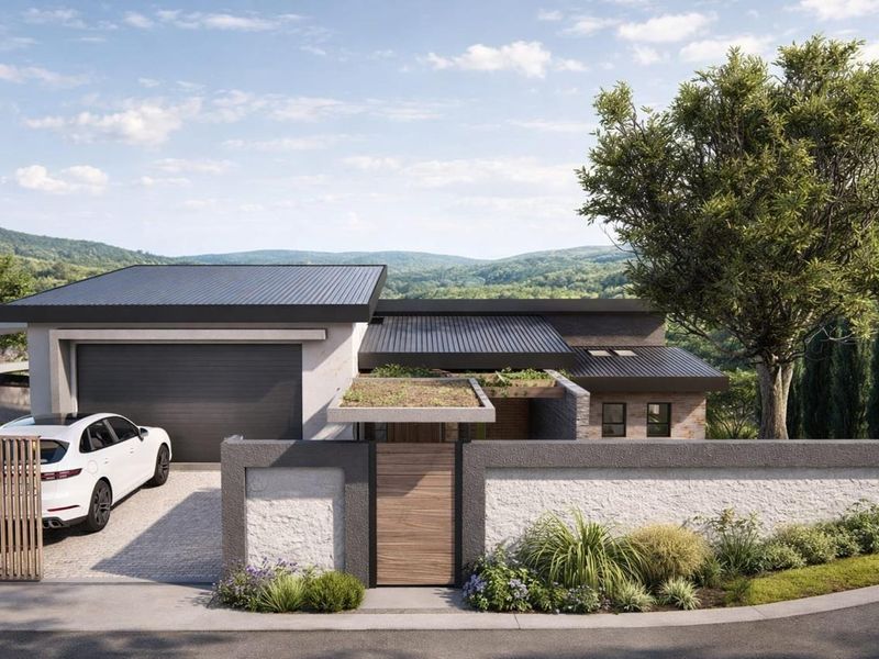Modern residential facade featuring a sleek metal roof, integrated garage, stone-textured boundary wall, and a timber entrance gate set against a scenic landscape.