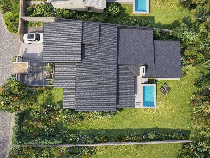 Aerial view of a residential property featuring a modern home with a tiled roof, private swimming pool, and landscaped garden.