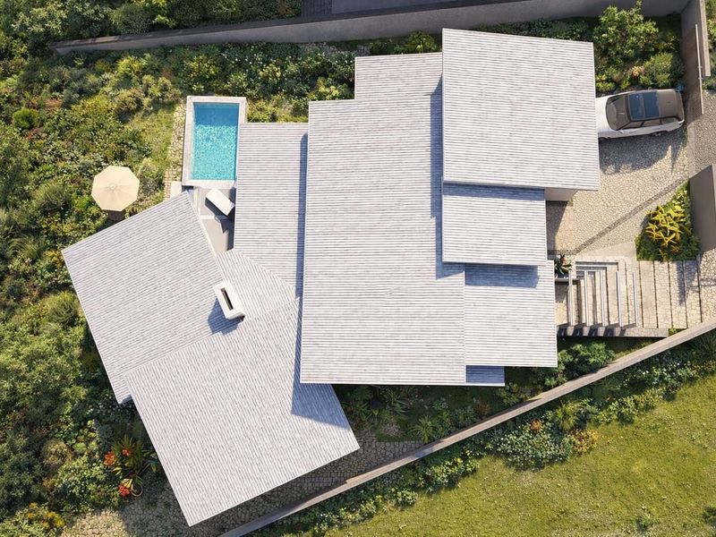 An aerial view of a modern residential property featuring a multi-level roof design, a private swimming pool, and landscaped garden areas.