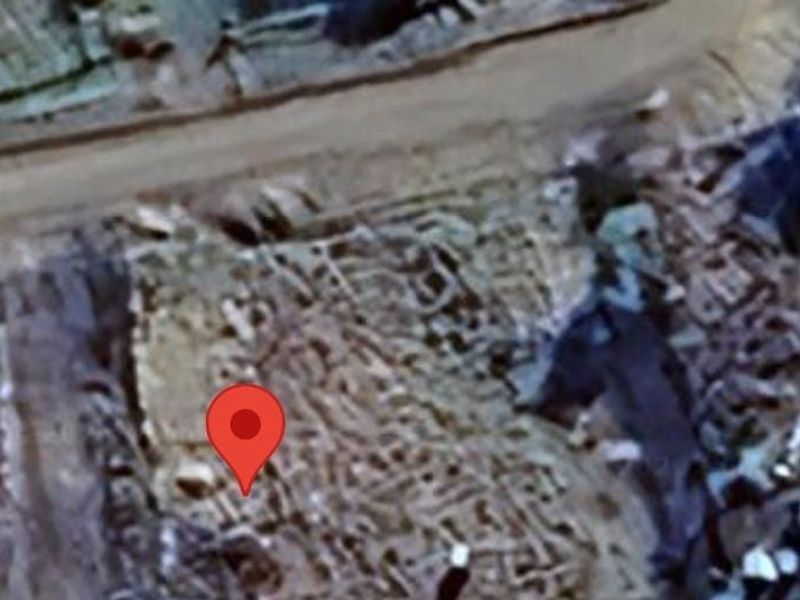 An aerial view of a vacant residential plot showing the surrounding terrain and access road.