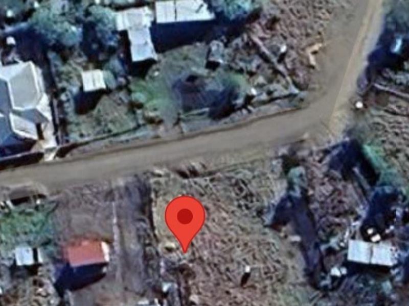 An aerial view of a vacant residential plot showing surrounding neighborhood context and access to the local dirt road.