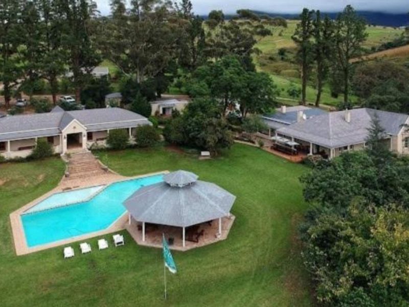 Aerial view of a residential property featuring multiple buildings, a swimming pool, a gazebo, and expansive landscaped grounds in a scenic setting.
