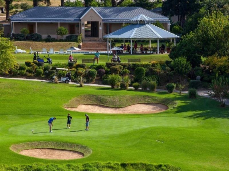 A scenic elevated view overlooking a well-maintained golf course, featuring sand bunkers, lush green fairways, and a clubhouse area with a pool and gazebo.