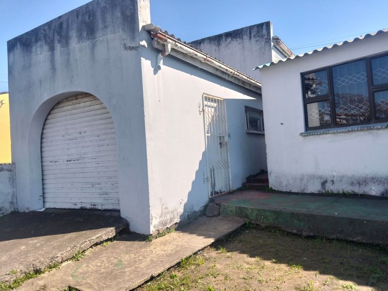 Front exterior view of the property featuring a garage with a roller door, security gate, and weathered concrete surfaces requiring maintenance.