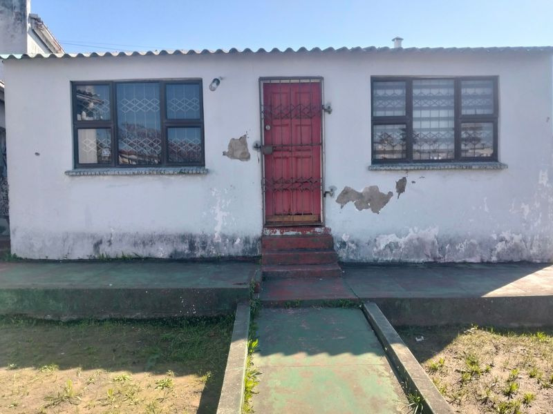 Front exterior view of a single-story house featuring a red security door, metal-framed windows with security bars, and a concrete entrance walkway.