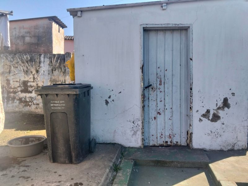 Exterior view of a rear utility structure featuring a metal door and concrete apron, showing significant signs of weathering and maintenance requirements.