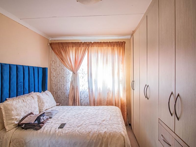 A functional bedroom featuring extensive built-in cupboards and natural light through window curtains.