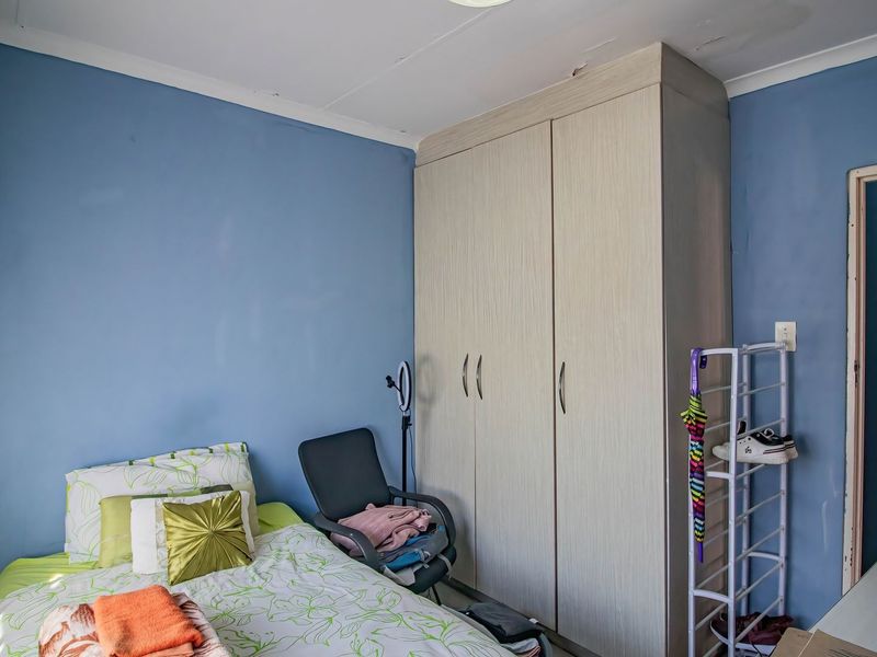 A bedroom featuring a built-in wardrobe and blue painted walls, showing signs of wear on the ceiling and wall surfaces.