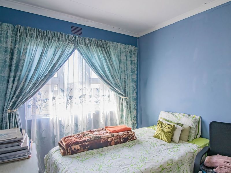 A standard bedroom featuring blue painted walls, a window with curtains, and ceiling cornicing.