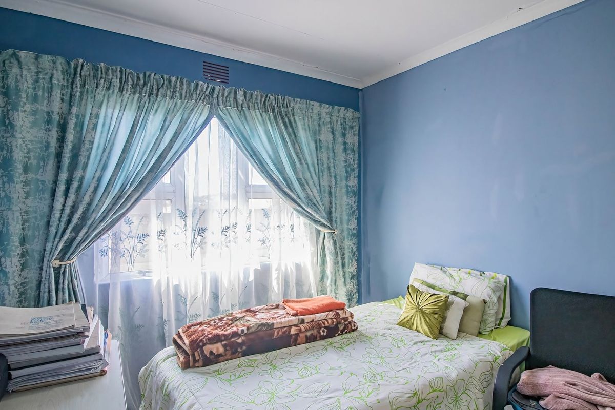 A standard bedroom featuring blue painted walls, a window with curtains, and ceiling cornicing.